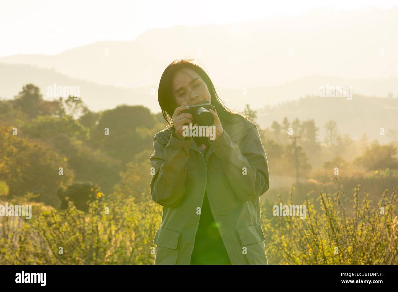 Junge asiatische Fotografin, die die Natur in sanfter Abendsonne einfängt und Outdoor-Fotografie genießt. Stockfoto