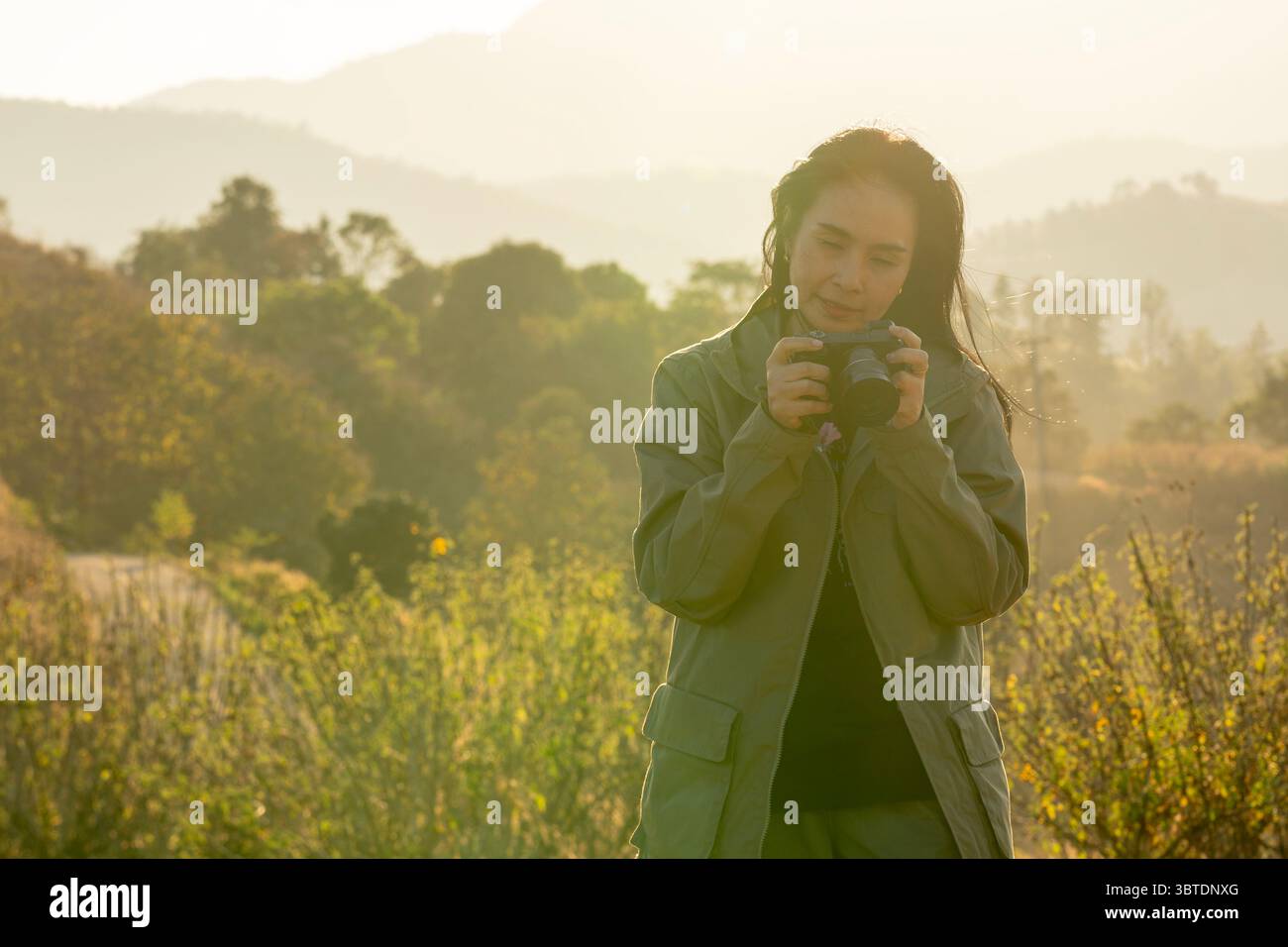 Junge asiatische Fotografin, die die Natur in sanfter Abendsonne einfängt und Outdoor-Fotografie genießt. Stockfoto
