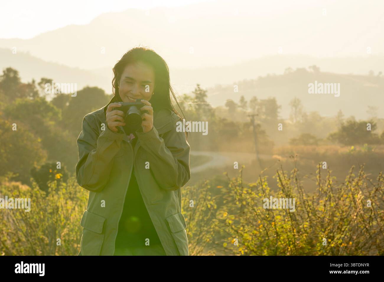 Junge asiatische Fotografin, die die Natur in sanfter Abendsonne einfängt und Outdoor-Fotografie genießt. Stockfoto