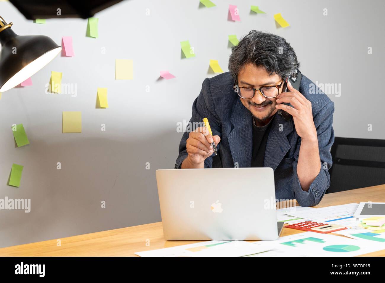 Ein lächelnder junger asiatischer Mann, der an seinem Schreibtisch arbeitet und ein positives und produktives Arbeitsumfeld genießt. Stockfoto