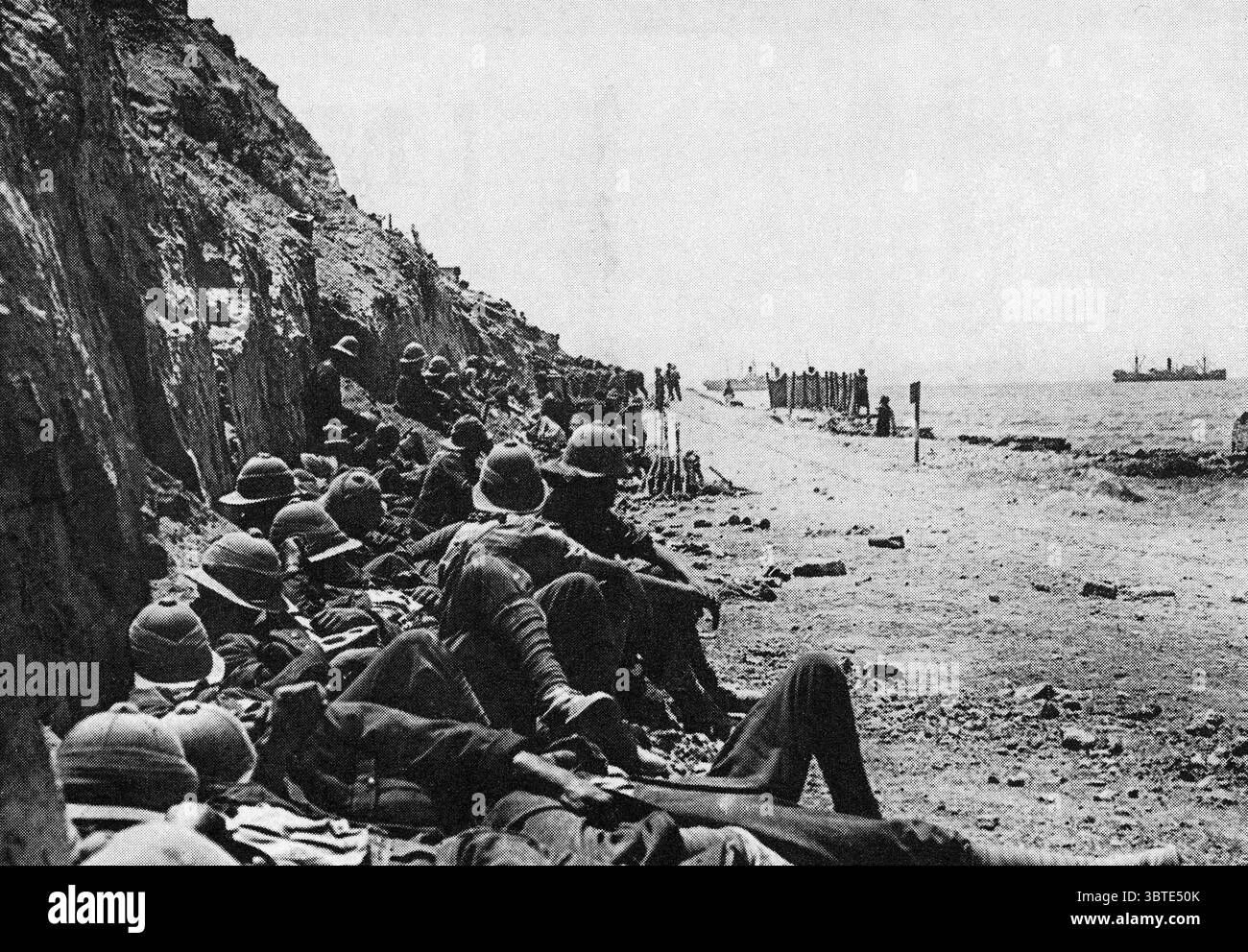Am Strand von Gallipoli hocken sich die britischen Tommies gegen die Klippe, um Schutz vor türkischem Bombardement zu bieten . Die Briten kämpften sich nie weit genug ins Landesinnere, um die Landungsstrände gegen feindliche Artillerie zu sichern, und türkische Scharfschützen schlängelten sich ständig durch die Linien, um die Briten in den Rücken zu schießen britische Truppen, die die Klippen am Kap Helles, Gallipoli umarmen, als eine Panzerung von der Türken 'Asiatic Annie' in der Nähe von - 1915 fällt Stockfoto