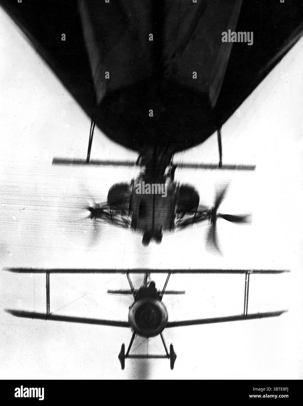 Ein Doppeldecker ( Nationalität unbekannt ), der nahe unter einer Gondel eines Luftschiffs unter dem wachsamen Auge der Kamera fliegt Stockfoto