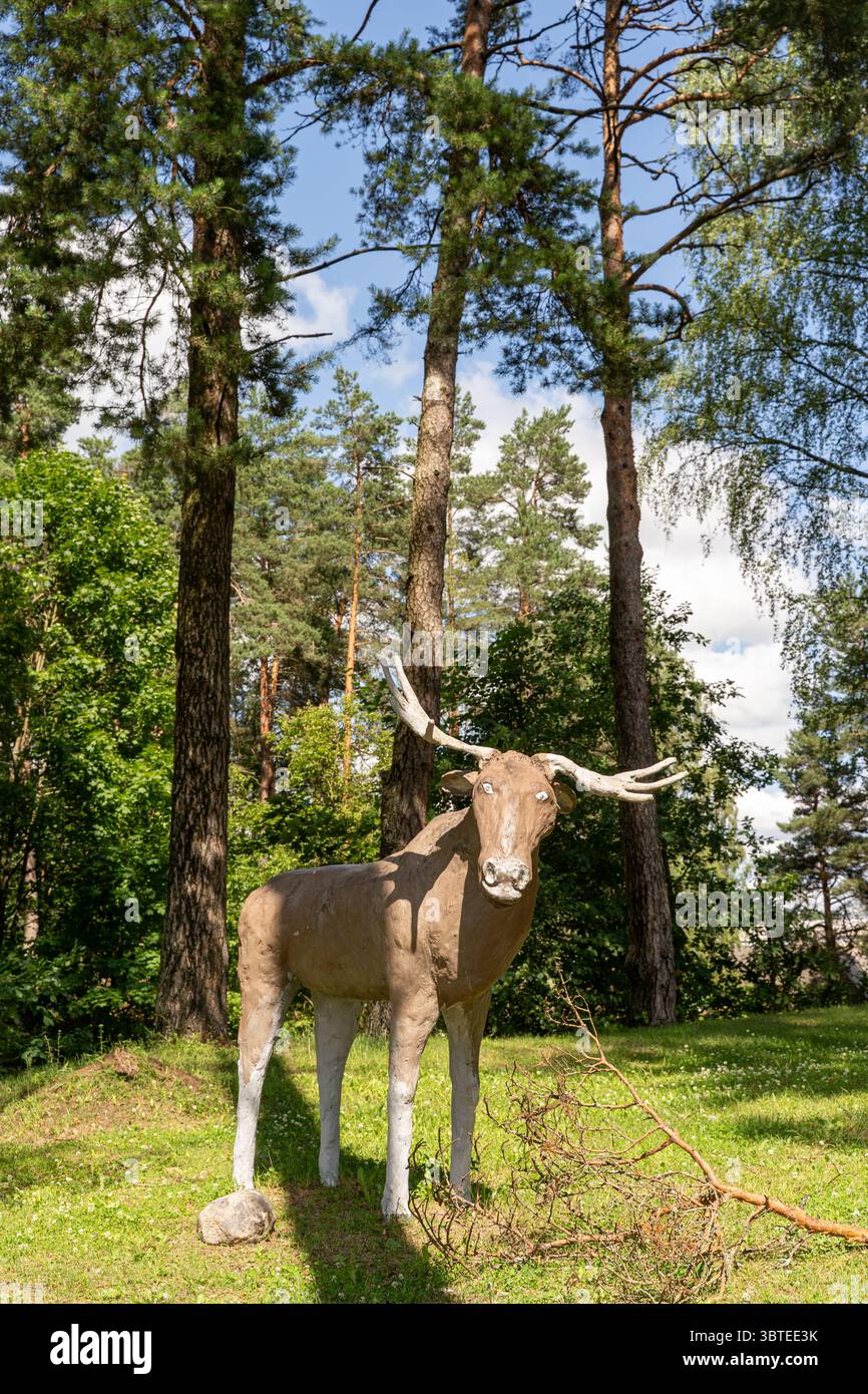 Skulptur eines Elchs mit naiven Augen, der zwischen Bäumen und Grün in Lasva, Võrumaa, Estland, steht – skurrile Kunst, die das Motiv der Tierwelt vereint Stockfoto