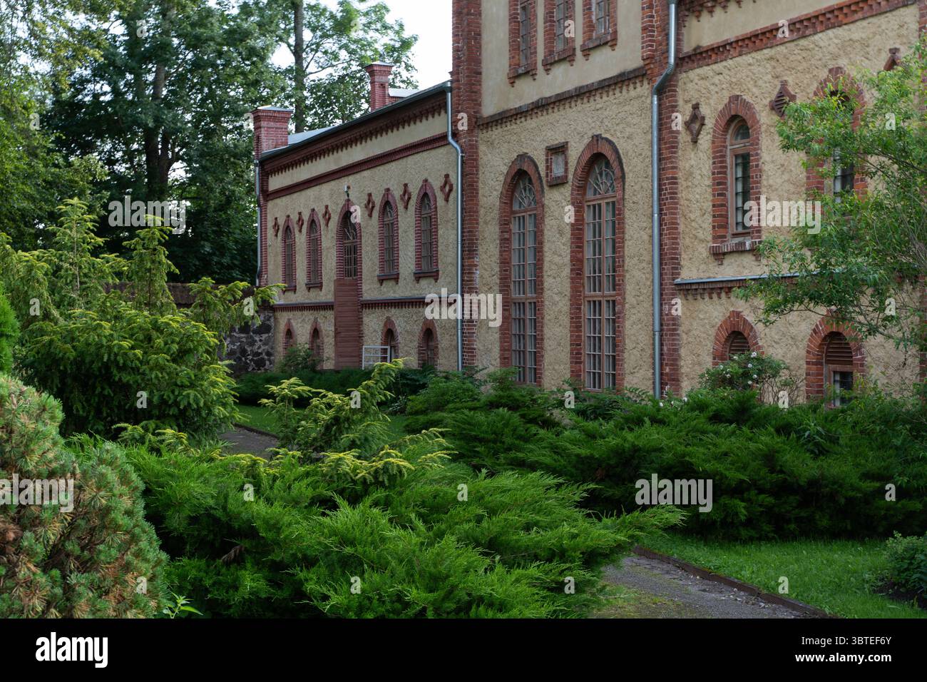 Nahaufnahme der bogenförmigen Fenster und dekorativen Ziegelmauerwerke auf dem Mooste Destillery Gebäude in Estland, umgeben von Grün und sanftem Licht Stockfoto
