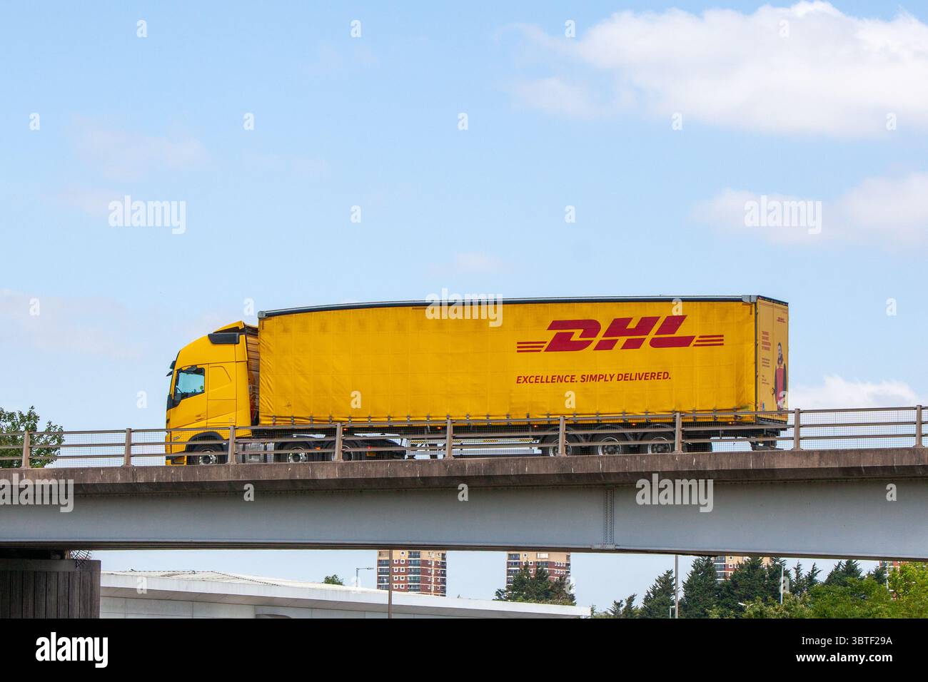 Ein gelber DHL Knickgelenkter Lkw mit Vorhangkante und „Excellence. Simply Delivered.“ Branding auf der Umgehungsstraße A5 in Tamworth, Großbritannien. Stockfoto
