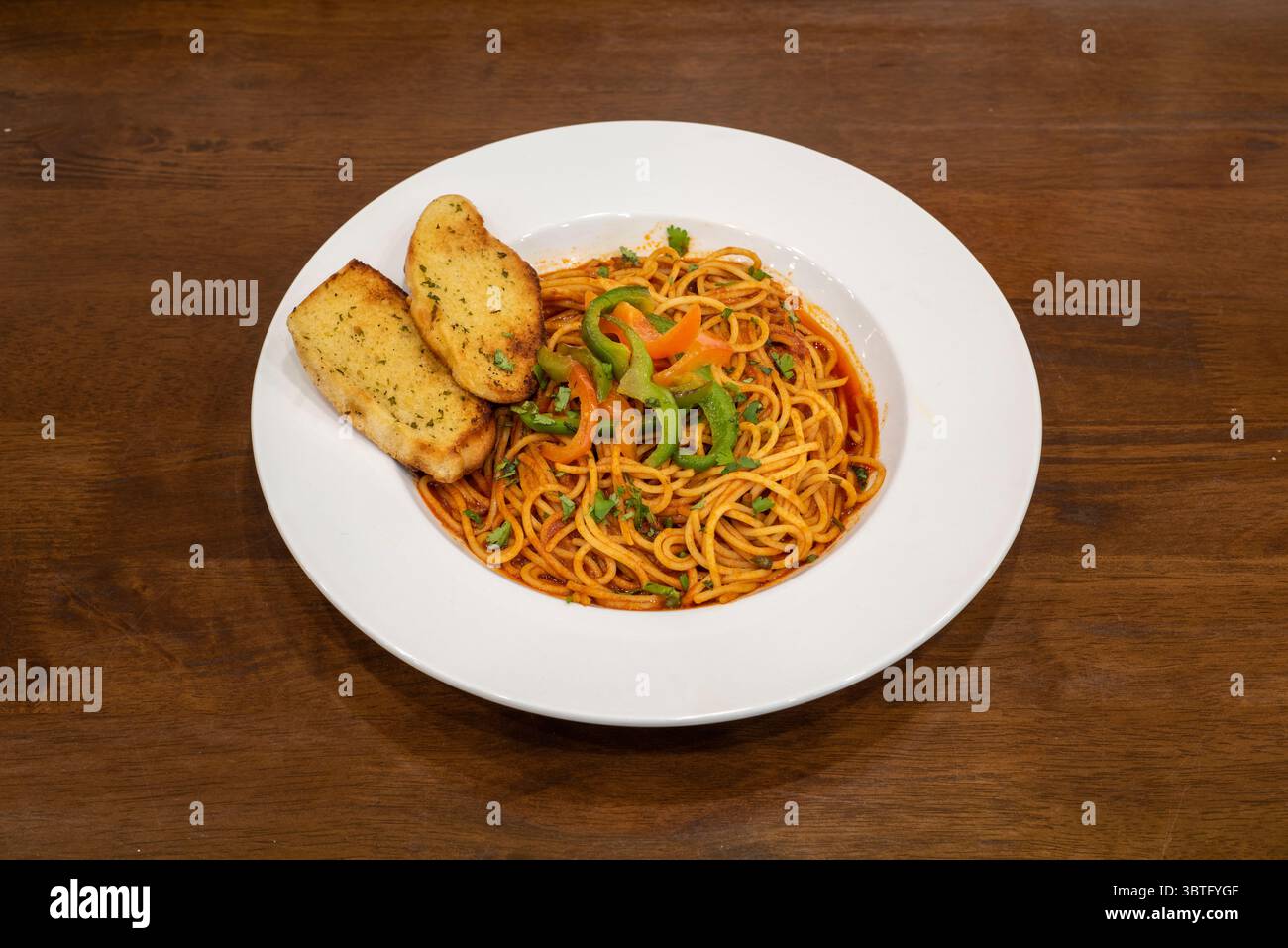 Spaghetti-Pasta in einer roten Tomatensauce, serviert mit zwei Scheiben Knoblauchbrot Stockfoto