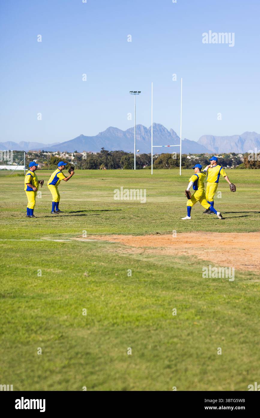 Männliche Baseballkameraden üben das Fliegen von Fly Ball auf dem Rasenfeld in der Nähe von weißen Rugby-Torpfosten Stockfoto