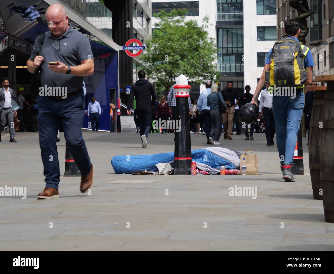 Moorfields, City of London, Großbritannien – Ein Obdachloser liegt in einem Schlafsack inmitten von gespendeten Lebensmitteln und Vorräten, die von Büroangestellten hinterlassen wurden. Dies veranschaulicht den starken Kontrast zwischen Reichtum und Armut im Finanzviertel Londons. Stockfoto Moorfields, City of London, Großbritannien – Ein Obdachloser liegt in einem Schlafsack inmitten von gespendeten Lebensmitteln und Vorräten, die von Büroangestellten hinterlassen wurden. Dies veranschaulicht den starken Kontrast zwischen Reichtum und Armut im Finanzviertel Londons. Stockfoto
