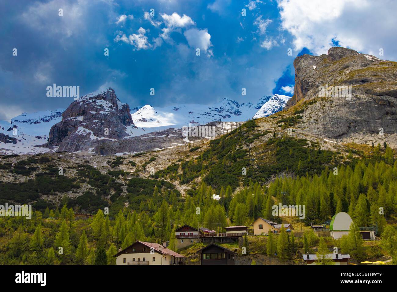 Die majestätischen schneebedeckten Gipfel der Marmolada überragen ein bezauberndes alpines Dorf inmitten üppiger grüner Wälder in den Dolomiten. Stockfoto