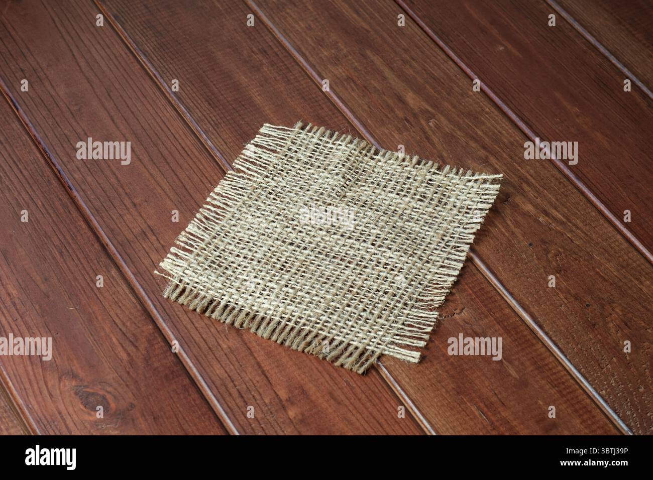 Ein strukturiertes Sackleinen-Quadrat auf poliertem Holz verleiht dem Zimmer rustikalen Charme. Stockfoto