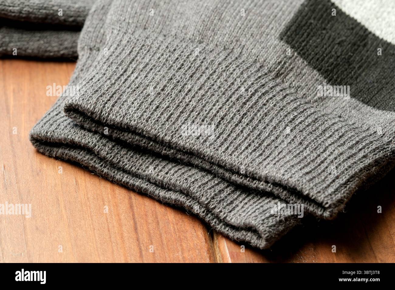 Strukturierte graue Ärmel liegen ordentlich auf einem Holztisch und sorgen für Wärme und Komfort. Stockfoto