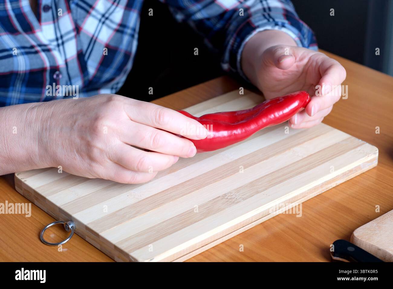 Hände einer älteren Frau, die rote Paprika in der Küche an einem braunen Tisch zeigt, ohne Gesicht, Nahaufnahme Stockfoto