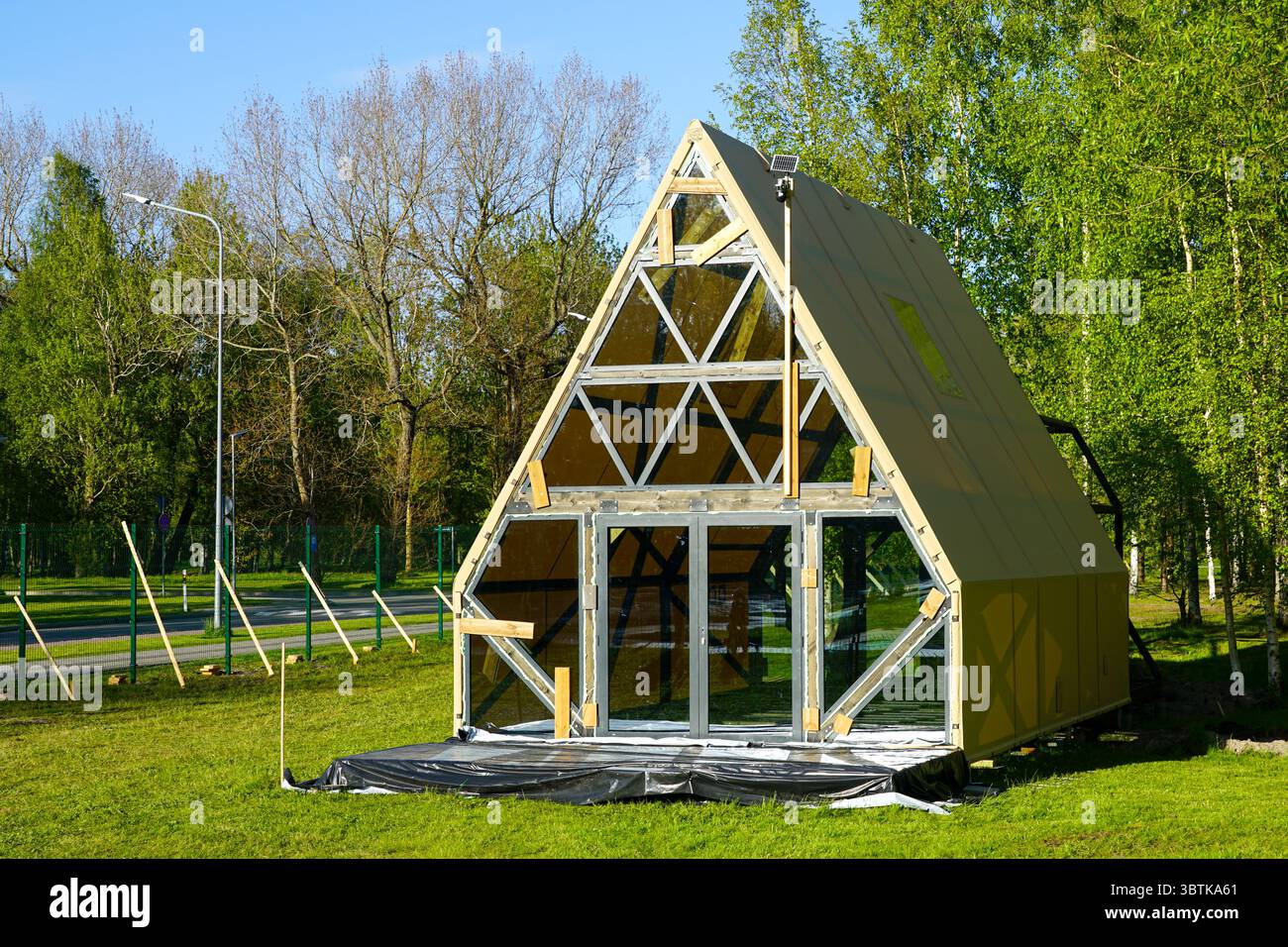 Ein einzigartiges dreieckiges Glamping-Haus im Bau, in einem üppig grünen Waldgebiet mit Glaswänden und Solarbeleuchtung Stockfoto