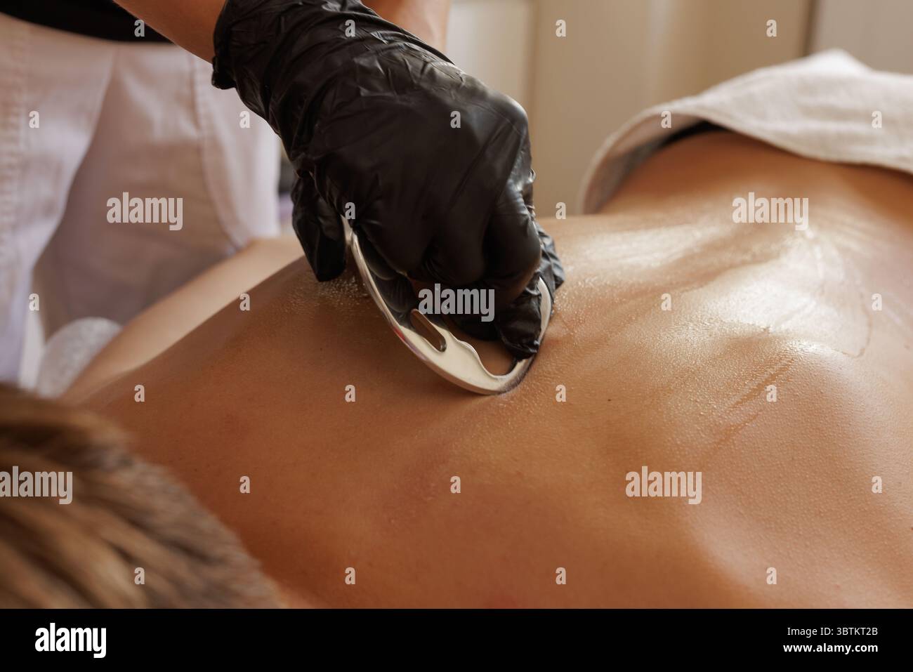 Ein professioneller Therapeut verwendet einen Metallschaber für die myofasziale Freisetzung und Wiederherstellung von Weichteilen in einer klinischen Umgebung Stockfoto