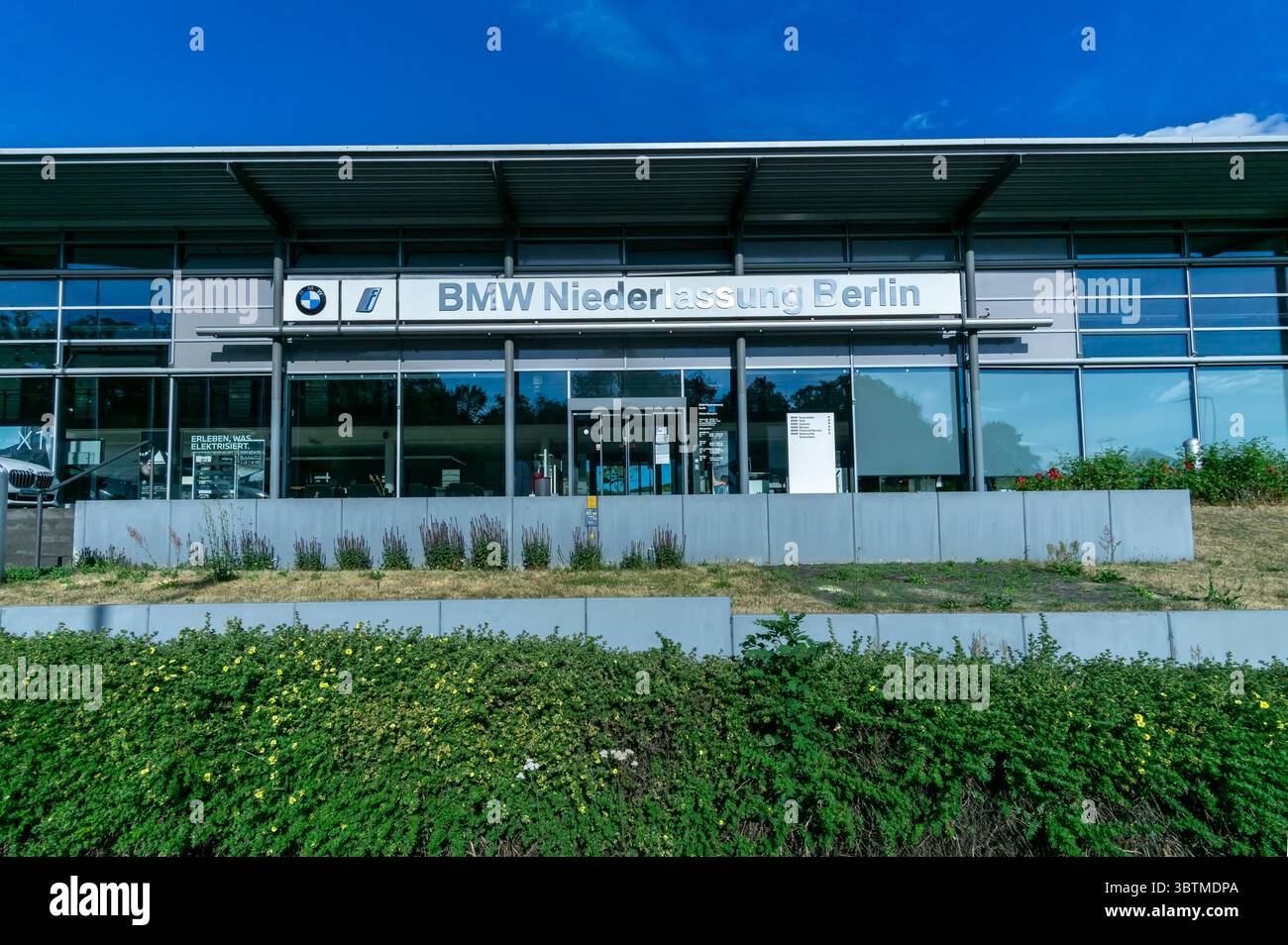 Exterieur BMW Händlerbetrieb Berlin Marzahn, moderne Glasfassade mit klarem blauem Himmel und grünen Pflanzen im Vordergrund. Stockfoto