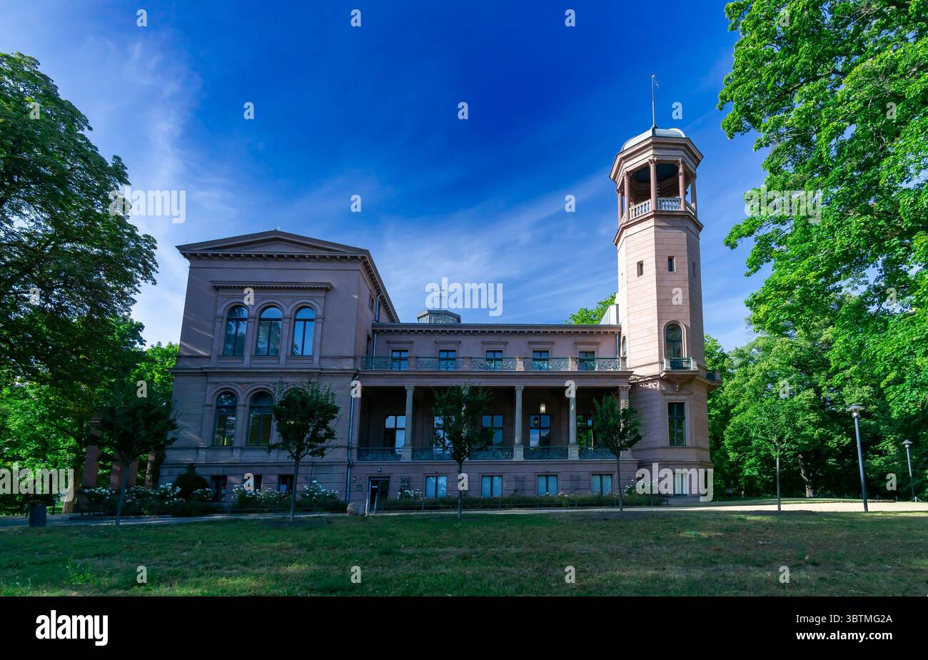Schloss Biesdorf in Berlin an einem hellen Sommertag, umgeben von grünen Bäumen und blauem Himmel, vom Vorgarten aus gesehen. Stockfoto