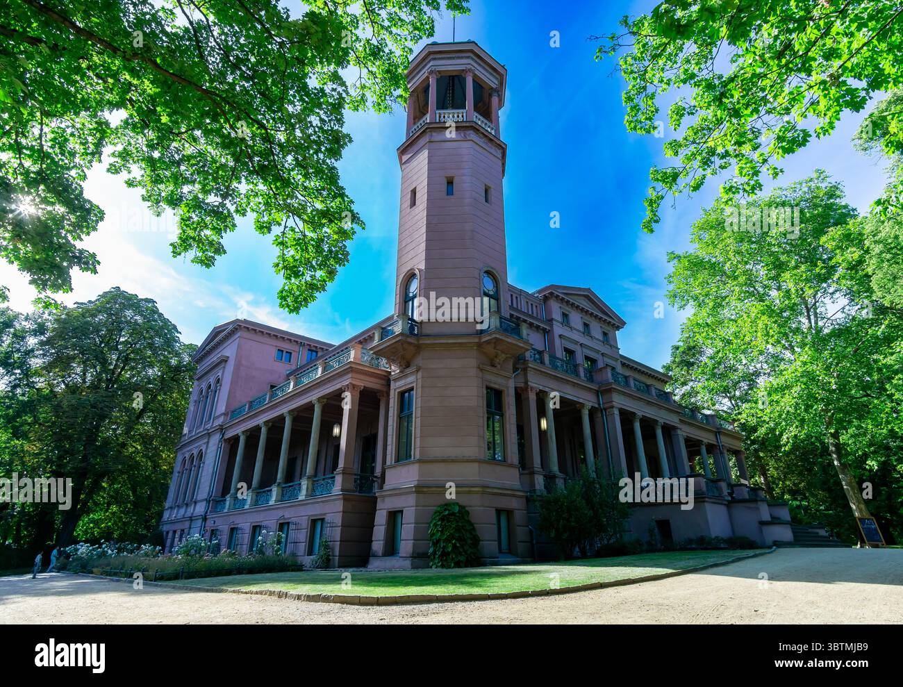 Schloss Biesdorf mit seinem berühmten Turm und Garten in Berlin an einem hellen Sommertag, umgeben von grünen Bäumen und klarem blauen Himmel. Stockfoto
