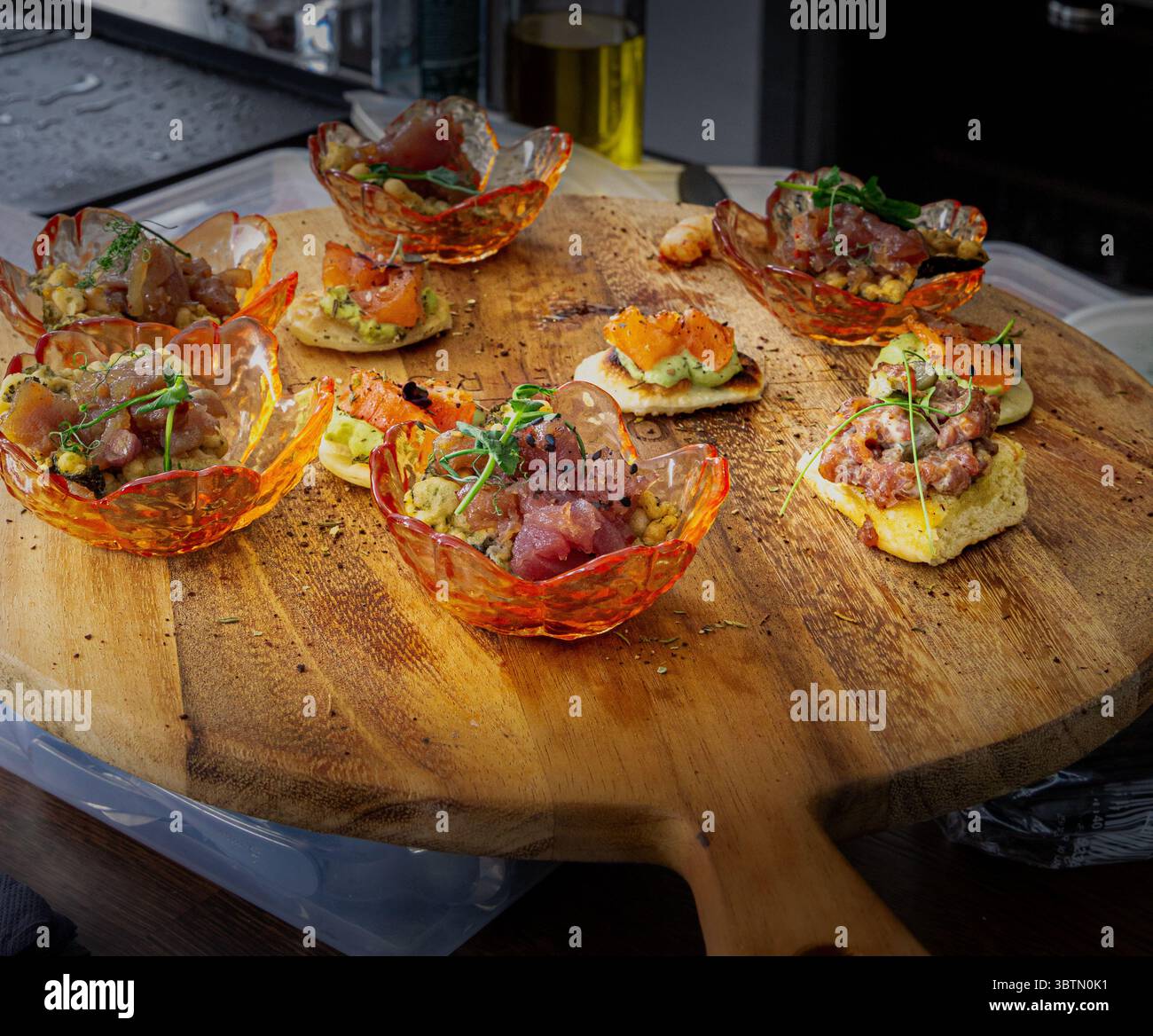Farbenfrohe Gourmet-Häppchen, darunter Thunfisch-Tatar und frische Kräuter, kunstvoll auf einem rustikalen Holzbrett während einer kulinarischen Präsentation Stockfoto