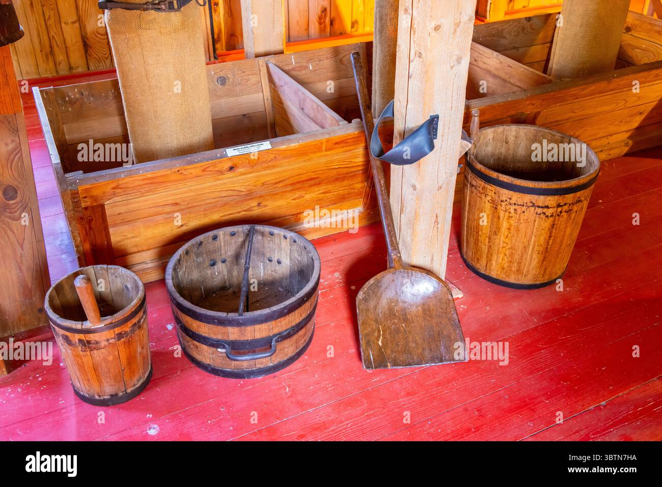 Das Innere einer alten Wassermühle mit Holzeimern, Schaufel und rotem Boden Stockfoto