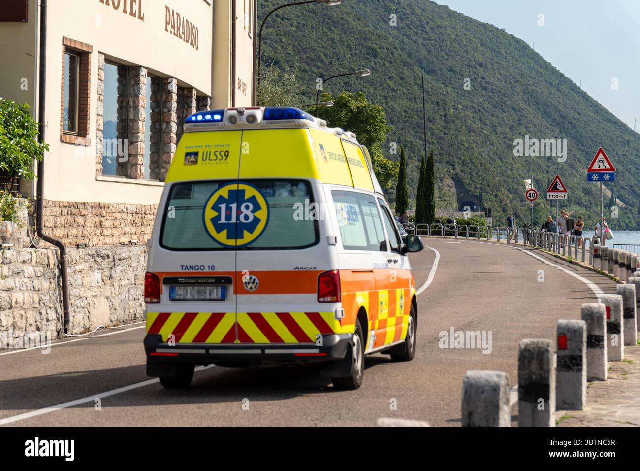 Nago-Torbole, Trentino, Italien - 15. Juli 2025: Ein italienischer Krankenwagen mit blauem Blinklicht ist auf dem Weg zu einer Operation in Torbole am Gardasee. Das Fahrzeug trägt die Notrufnummer 118 und gehört zum Regionalrettungsdienst ULSS 9 in Veneto *** ein italienischer Krankenwagen mit Blaulicht ist auf dem Weg zu einem Einsatz in Torbole am Gardasee. Das Fahrzeug trägt die Notrufnummer 118 und gehört zum regionalen Rettungsdienst ULSS 9 in Venetien Stockfoto