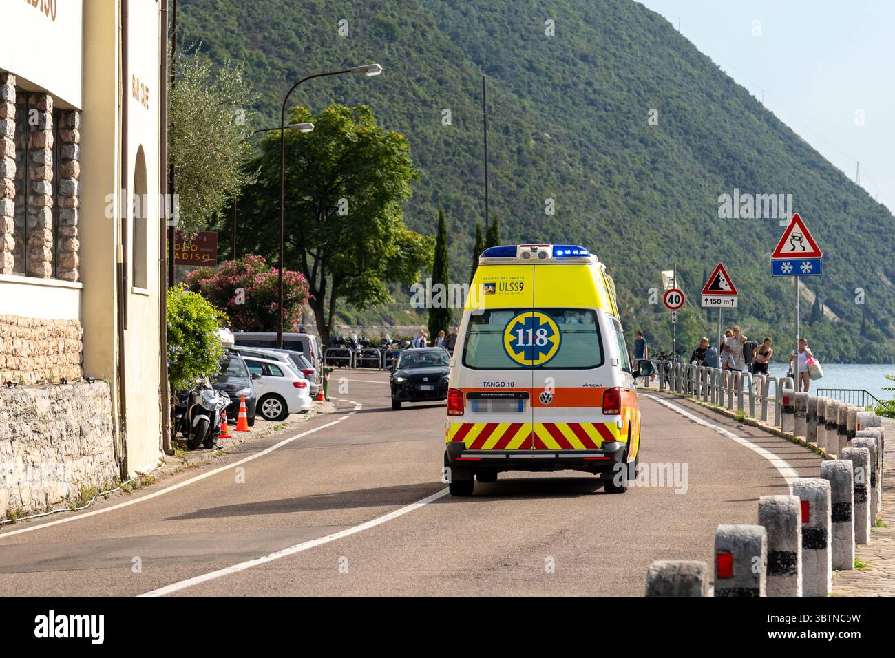 Nago-Torbole, Trentino, Italien - 15. Juli 2025: Ein italienischer Krankenwagen mit blauem Blinklicht ist auf dem Weg zu einer Operation in Torbole am Gardasee. Das Fahrzeug trägt die Notrufnummer 118 und gehört zum Regionalrettungsdienst ULSS 9 in Veneto *** ein italienischer Krankenwagen mit Blaulicht ist auf dem Weg zu einem Einsatz in Torbole am Gardasee. Das Fahrzeug trägt die Notrufnummer 118 und gehört zum regionalen Rettungsdienst ULSS 9 in Venetien Stockfoto