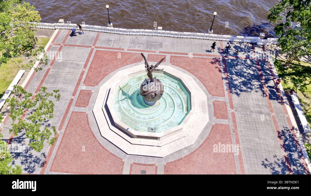 Aus der Vogelperspektive einer Skulptur eines geflügelten Engels, der auf einem Globus-Brunnen auf einem Backsteinplatz in der Nähe des Wassers steht, Jacksonville, Florida, USA. Stockfoto