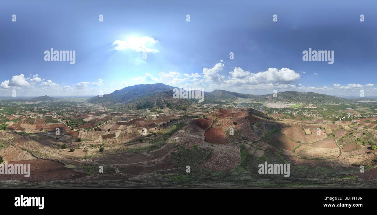 Aus der Vogelperspektive von landwirtschaftlichen Flächen mit rotem Boden im Kontrast zu den grünen Bergketten unter Wolken, Chu PAH, Gia Lai, Vietnam. Stockfoto