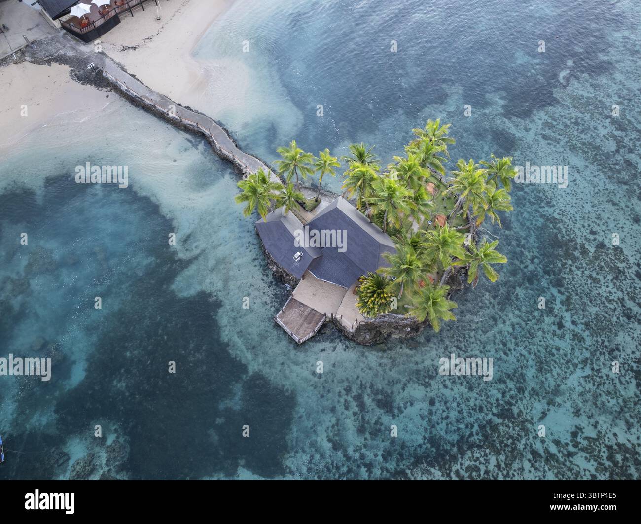 Blick aus der Vogelperspektive auf eine abgelegene Insel mit einer Villa mit dunklem Dach, umgeben von türkisfarbenem Wasser und lebhaften Palmen, Korolevu, Korolevu, Fidschi. Stockfoto