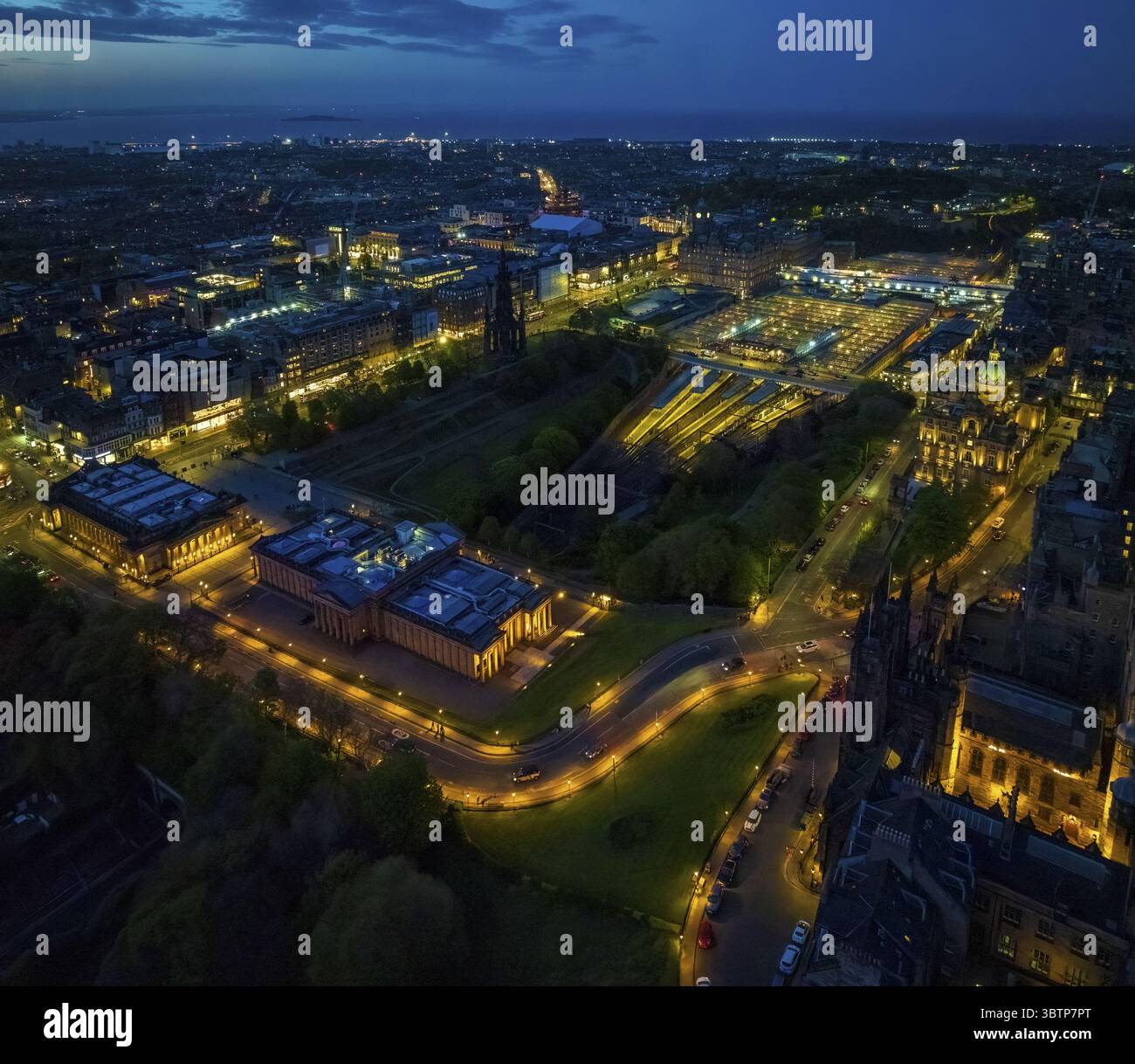 Blick aus der Vogelperspektive auf die Stadt bei Nacht, gebadet in das warme Licht der Straßenlaternen, die sich durch die Parks schlängeln und die großen Gebäude in Honigtönen vor dem dunkelblauen Himmel erleuchten, Edinburgh, Schottland, Großbritannien. Stockfoto