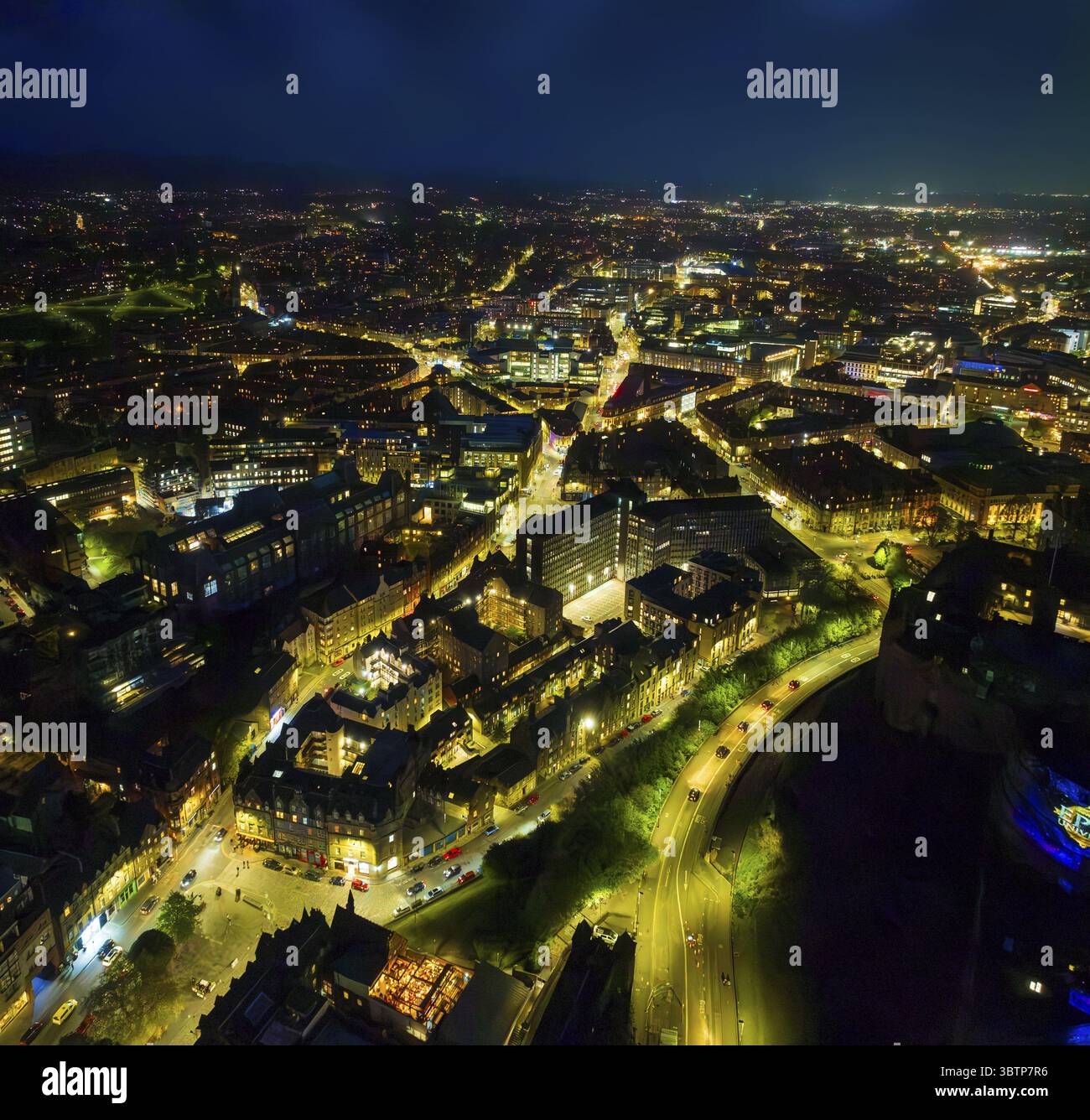 Luftaufnahme einer weitläufigen Stadtlandschaft, die unter dem Nachthimmel leuchtet, Straßen mit beweglichen Autos und warmen Straßenlaternen, die lange Schatten werfen, und Gebäude unterschiedlicher Größe und Höhe beleuchten, Edinburgh, Schottland, Großbritannien. Stockfoto