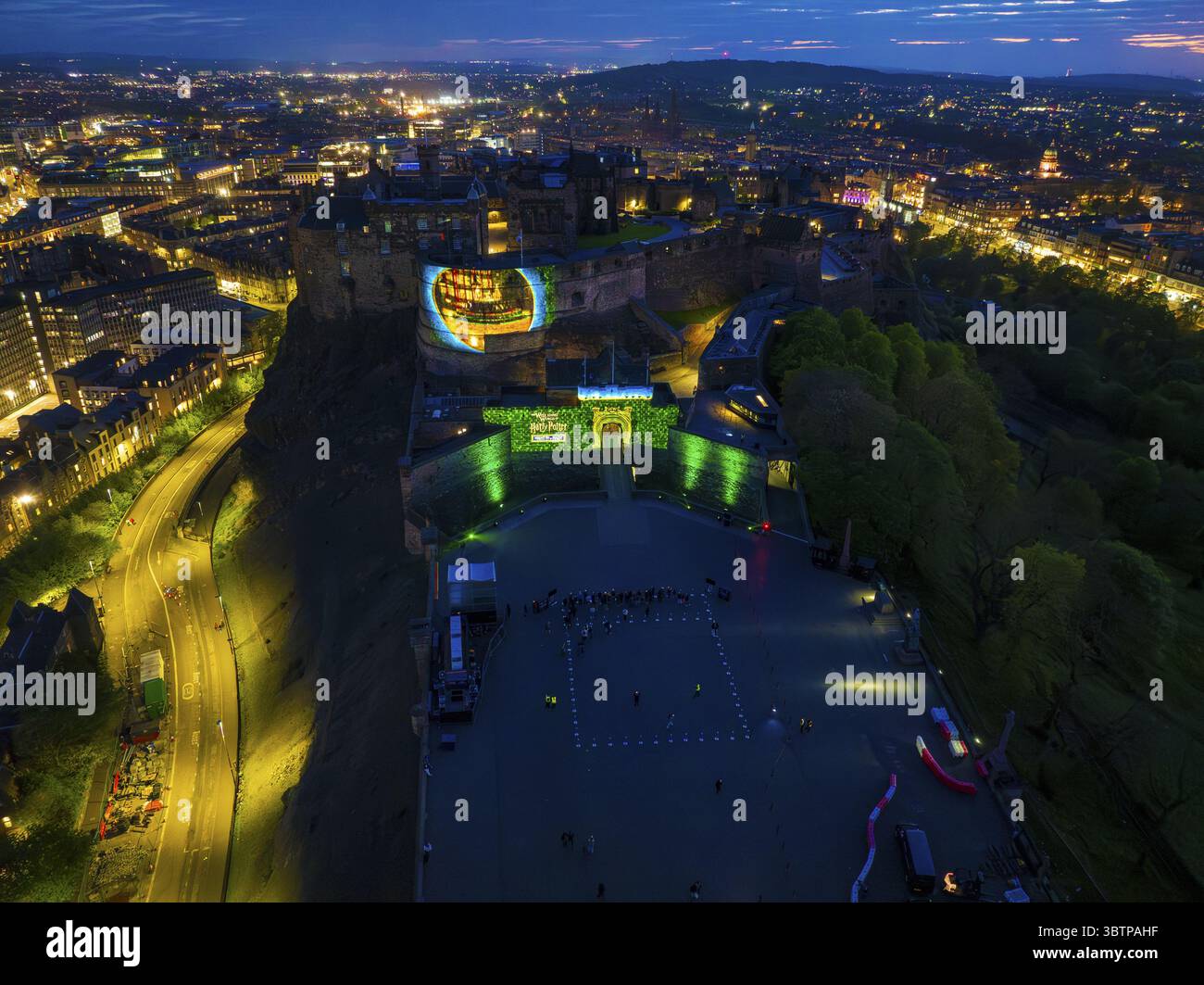 Edinburgh, Großbritannien - 16. Juni 2025: Aus der Vogelperspektive eine pulsierende Stadtlandschaft, in der Edinburgh Castle mit lebhaften Projektionen beleuchtet wird, seine alten Steine gegen den Dämmerhimmel leuchten, die lebendigen Grün- und Blautöne einen scharfen Kontrast zu den warmen Lichtern der Stadt bilden, die sich durch die urbane Landschaft schlängeln, ein dynamisches Zusammenspiel von Geschichte und Moderne. Stockfoto