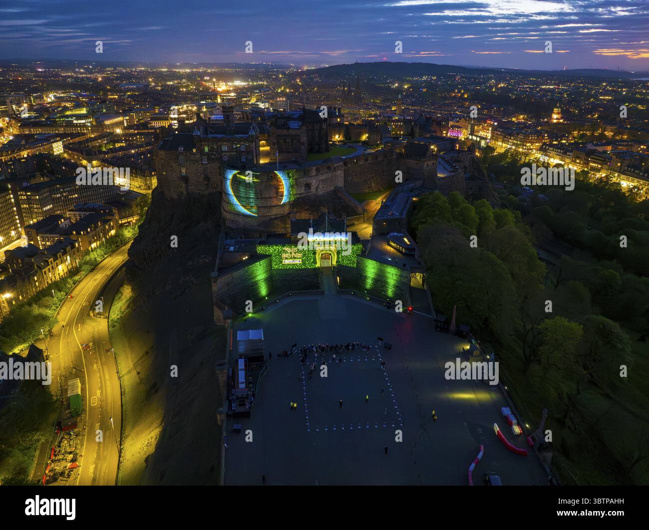 Edinburgh, Vereinigtes Königreich - 16. Juni 2025: Aus der Luft erhebt sich Edinburgh Castle majestätisch auf seinem vulkanischen Felsen, getaucht in sanftem Licht der Dämmerung und leuchtenden Lichtern, was einen dramatischen Kontrast zu der dunklen Stadtlandschaft darunter schafft. Stockfoto