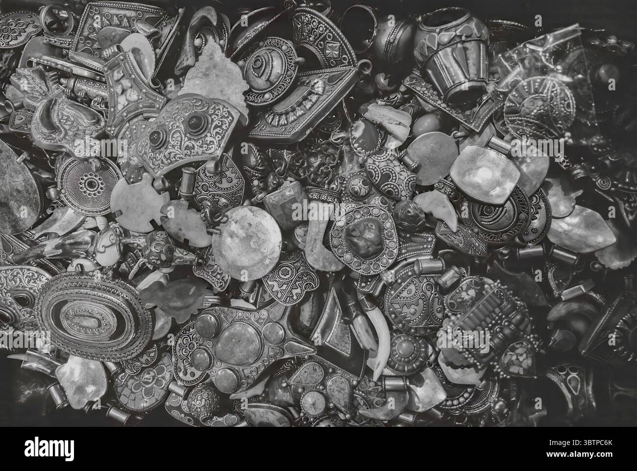Nahaufnahme verschiedener traditioneller Metallschmuckstücke in Schwarz-weiß. Aufwändig gefertigte Anhänger, Perlen und Ornamente. Stockfoto