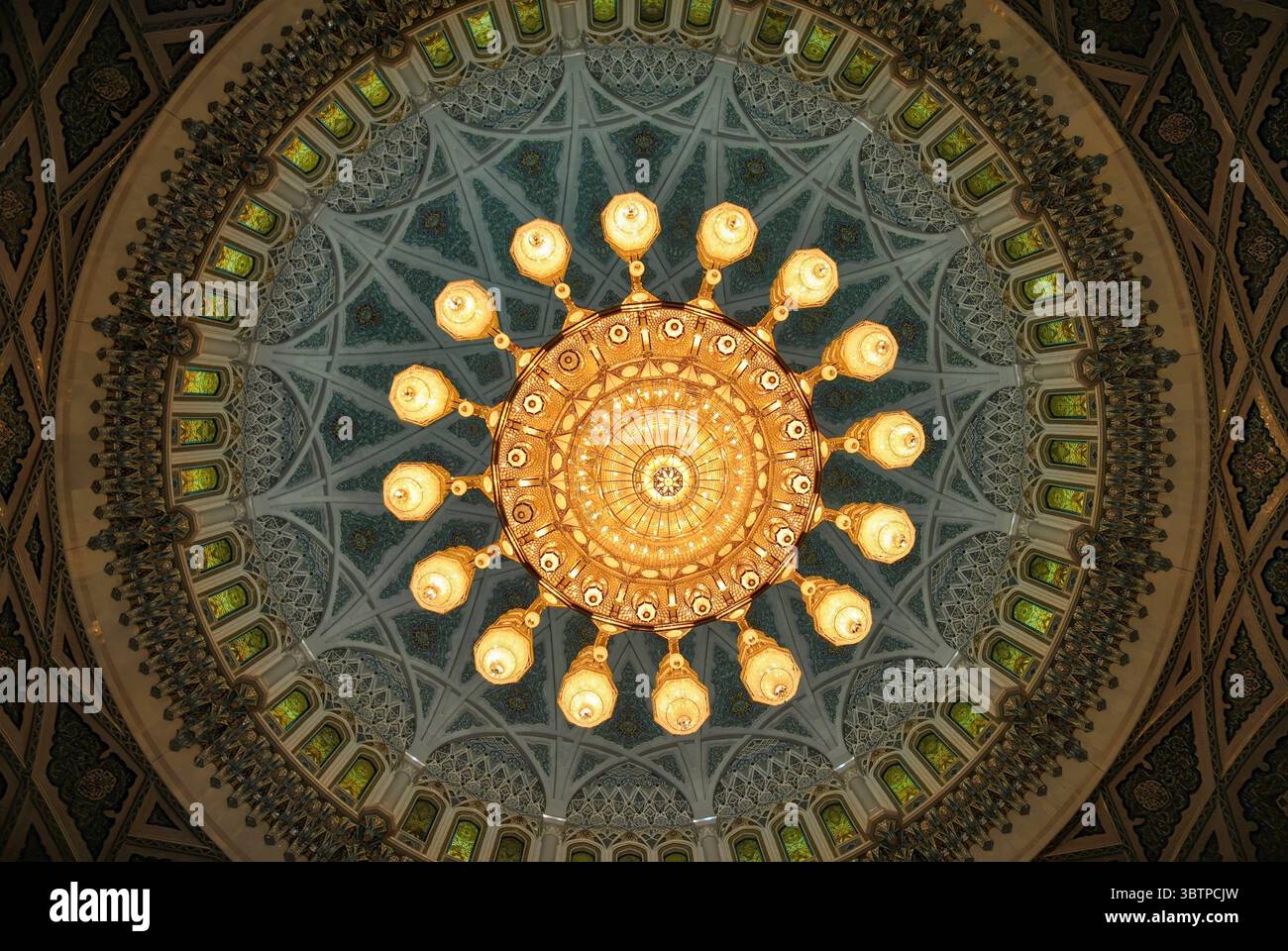 Blick auf einen großen, reich verzierten Kronleuchter in einer reich verzierten Moschee Kuppel. Symmetrische islamische Architektur mit Buntglasfenstern. Stockfoto