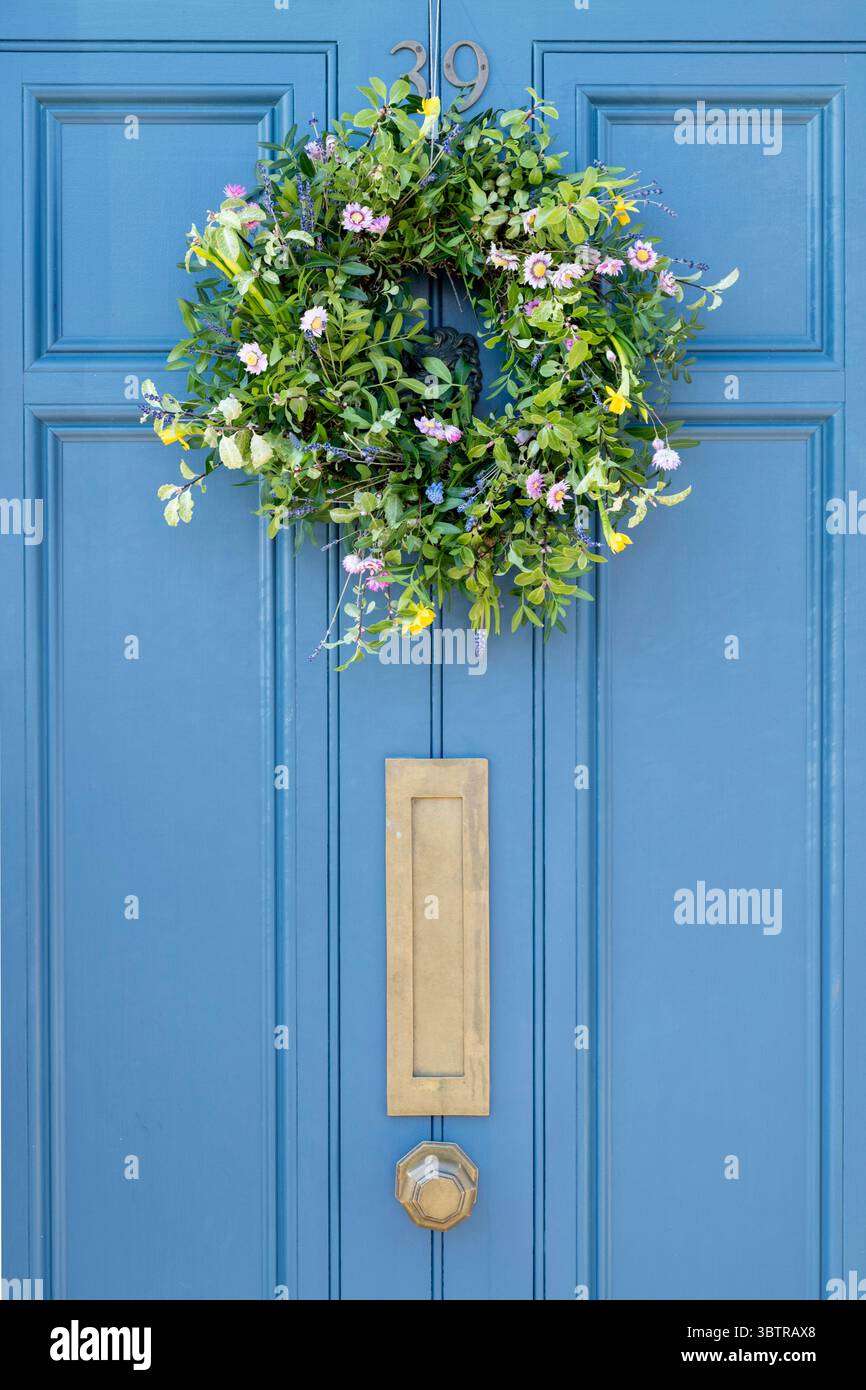 Elegante blau lackierte Tür mit einem Kranz aus Frühlingsblumen im traditionellen, malerischen Dorf Sherston in Wiltshire, England, Großbritannien Stockfoto