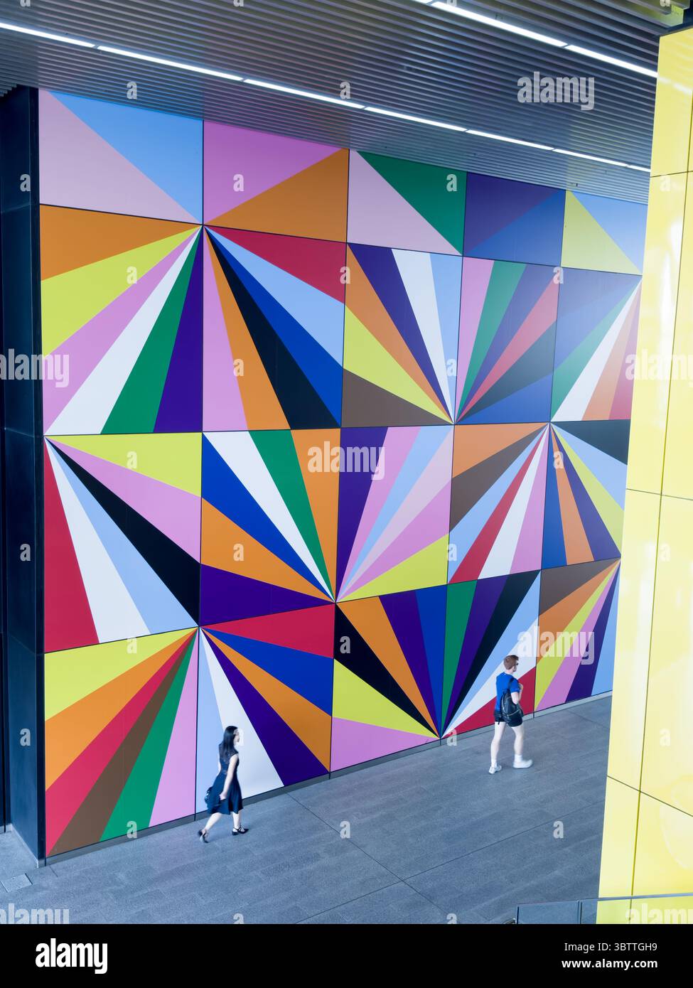 Ein Pendler spaziert an einer lebendigen, mehrfarbigen geometrischen Kunstinstallation in Canary Wharf Crossrail Station in London, Großbritannien vorbei. Stockfoto