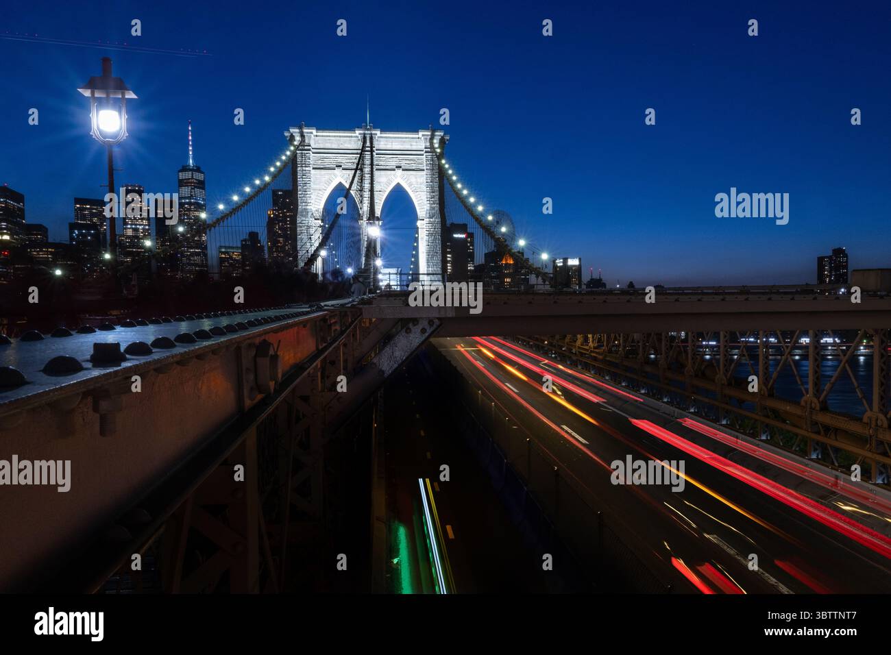 Brooklyn Bridge Traffic - Autos bei Sonnenuntergang Abend und Einbruch der Dunkelheit - Zeitverzögerungsbewegung verschwimmen Steinbögen in Lower Manhattan New York City mit Skyline Stockfoto