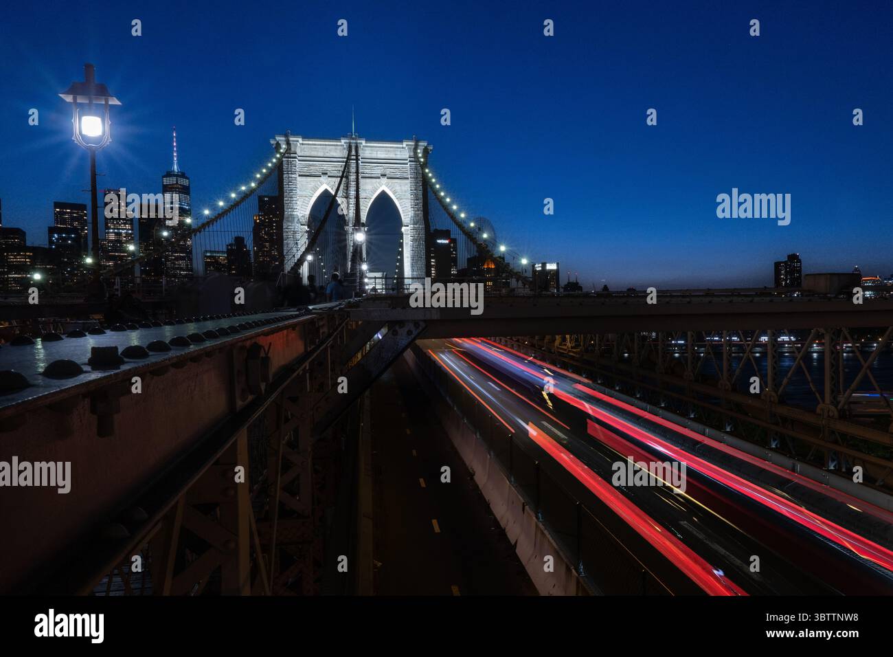 Brooklyn Bridge Traffic - Autos bei Sonnenuntergang Abend und Einbruch der Dunkelheit - Zeitverzögerungsbewegung verschwimmen Steinbögen in Lower Manhattan New York City mit Skyline Stockfoto