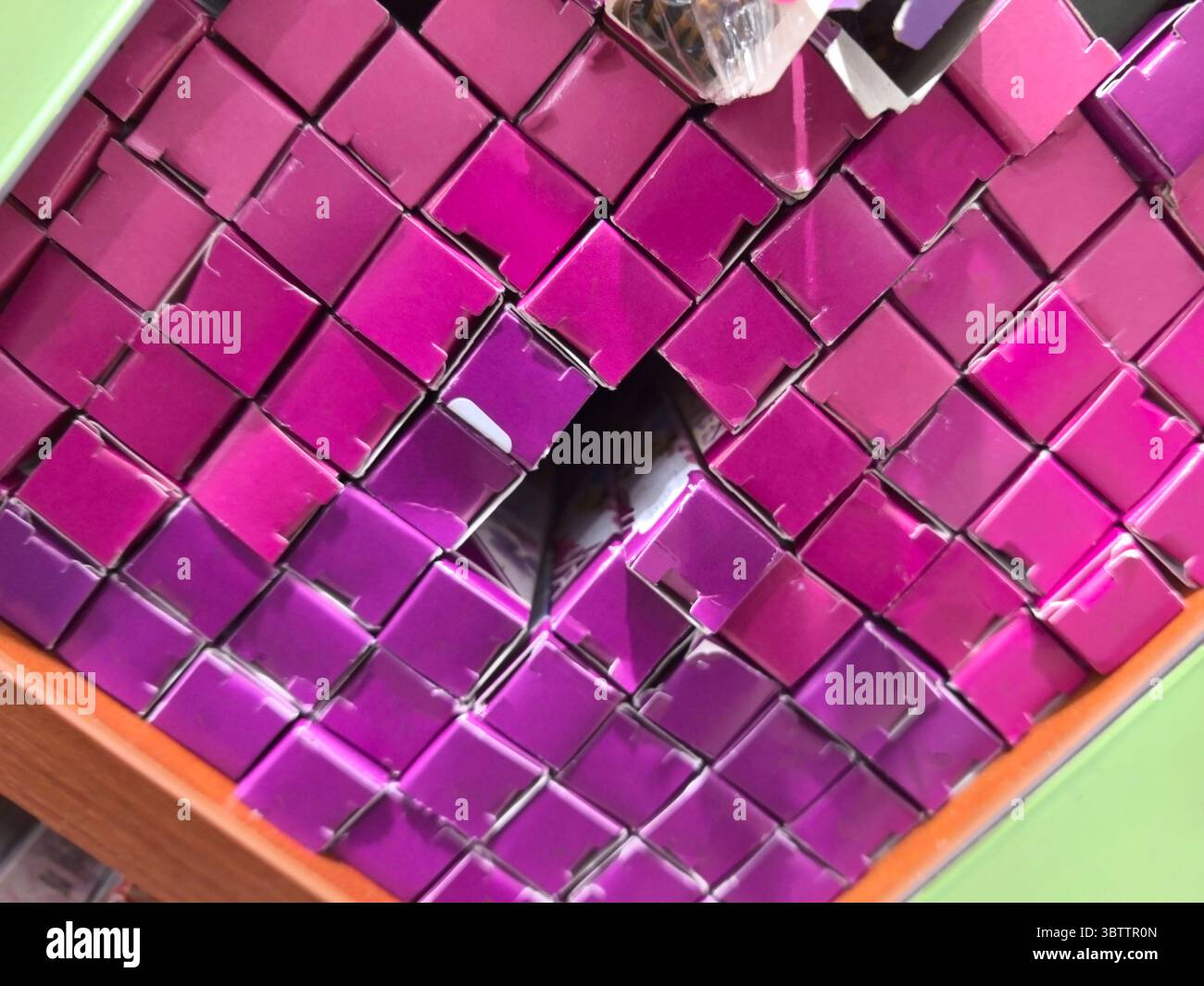 Eine Vielzahl von Schachteln in leuchtenden Rosa- und Violetttönen sind übereinander angeordnet. Das einzigartige Arrangement unterstreicht ein verspieltes und doch organisiertes PR Stockfoto