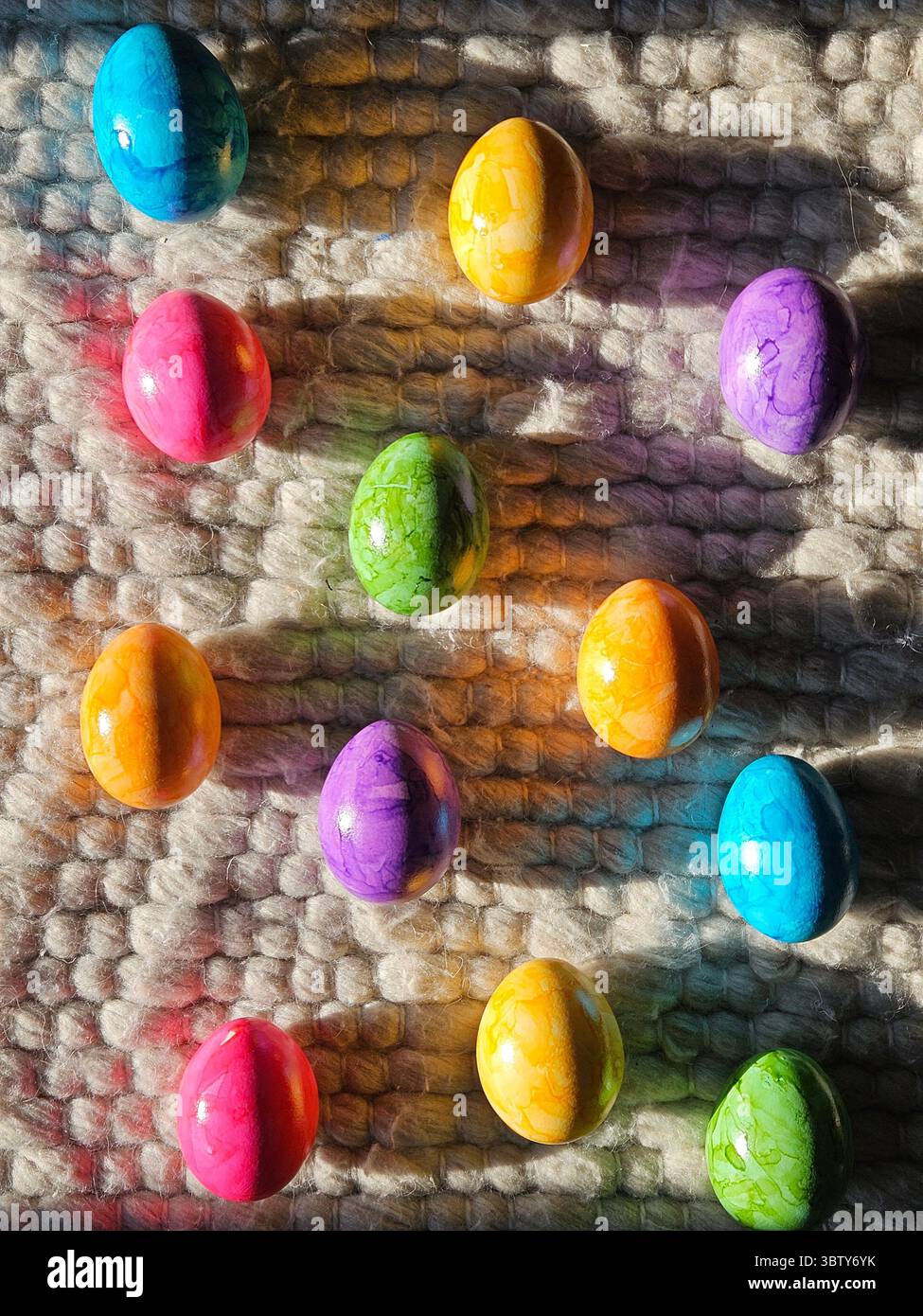 Bunte Ostereier auf strukturiertem Wollteppich im Sonnenlicht. Lebhafte Frühlingsferien im Hintergrund. Hochwertige Fotos Stockfoto