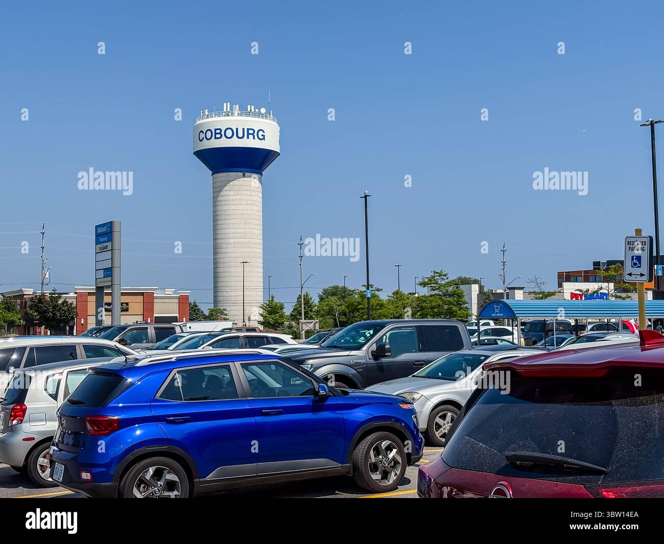 Cobourg Water Tower. Hohes Gebäude mit „COBOURG“-Text über einem Parkplatz mit Autos und Gebäuden in Cobourg, Ontario, Kanada. Stockfoto