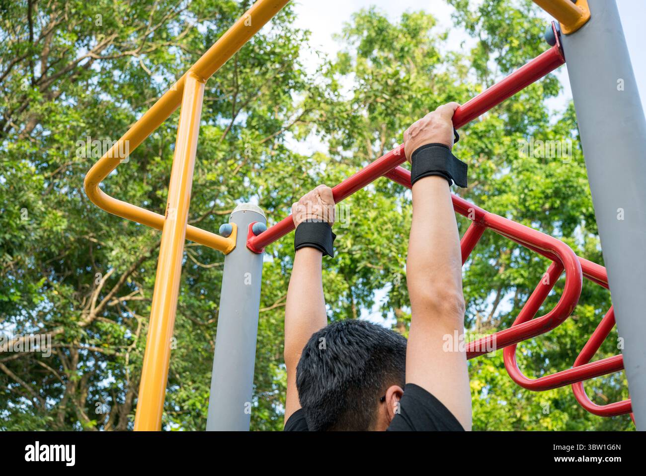 Ein Mann, der Klimmzüge auf der Stahlstange im Park macht. Rückansicht. Stockfoto