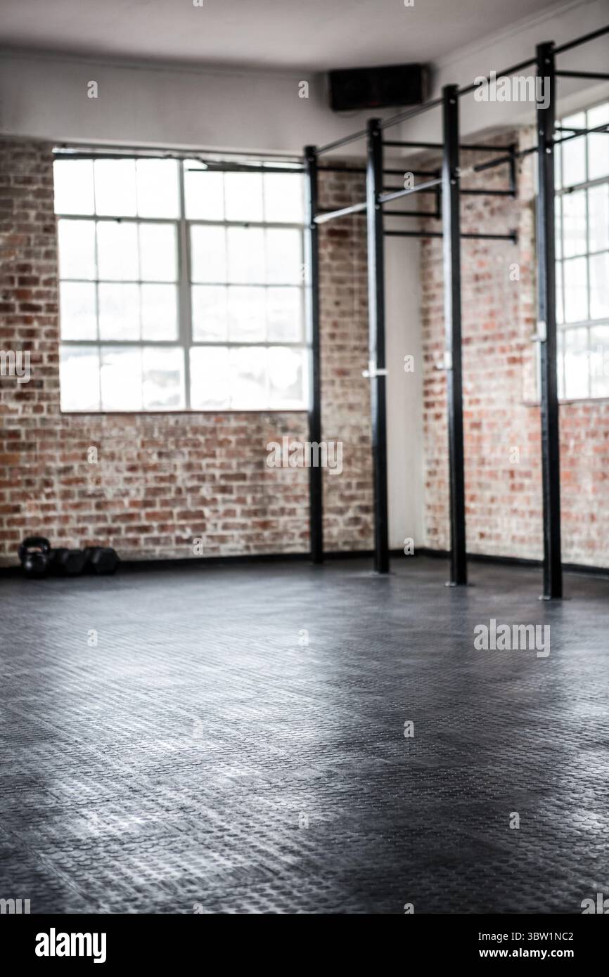 Das schwarze Pull-up-Bohrfahrzeug aus Stahl steht in einem flachen, aus Ziegeln gefertigten Fitnessstudio mit Kurzhanteln und Gummimatten Stockfoto