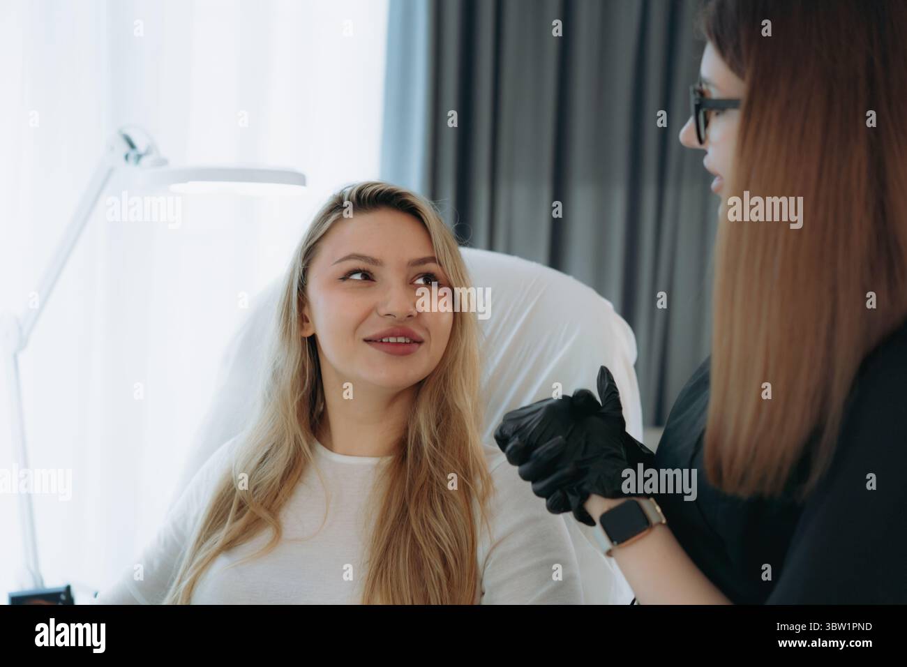 Frau vor der Faciumverjüngungsinjektion in der ästhetischen Klinik. Der Arzt erklärt das Vorgehen Stockfoto