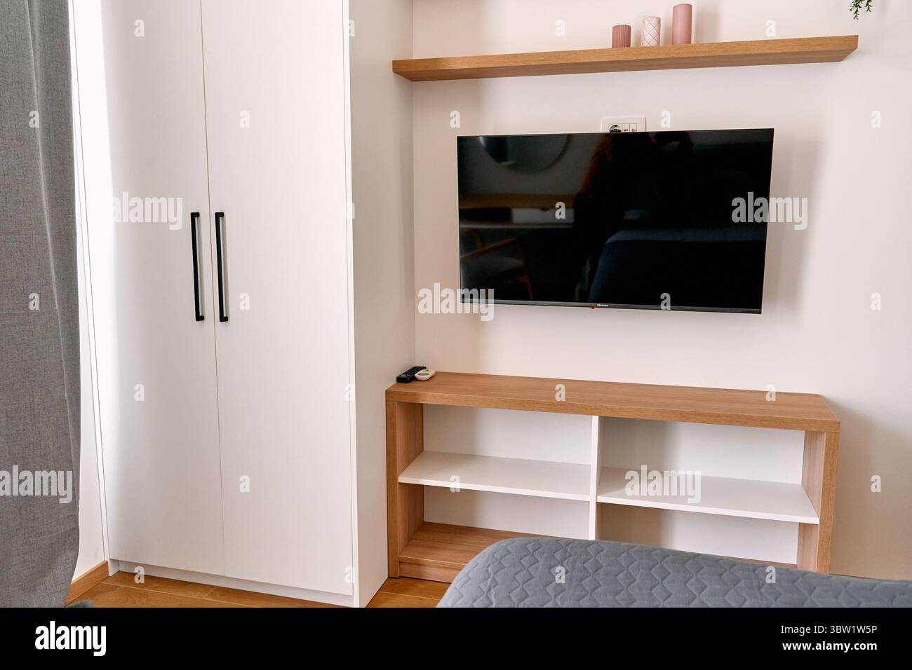 Das moderne Schlafzimmer verfügt über einen wandmontierten fernseher und minimalistischen Stauraum mit einem eleganten Kleiderschrank und offenen Regalen für ein organisiertes Wohnen. Stockfoto