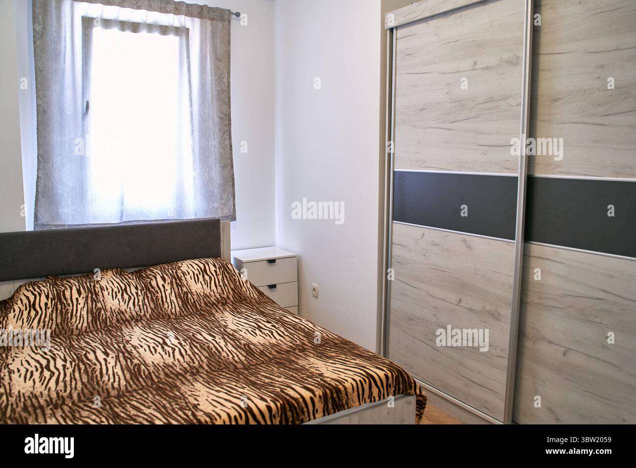 Ein gemütliches Schlafzimmer mit Tiermotiv und einem modernen Holzschrank. Der Raum verfügt über Tageslicht, eine minimalistische Einrichtung und eine ruhige Atmosphäre Stockfoto