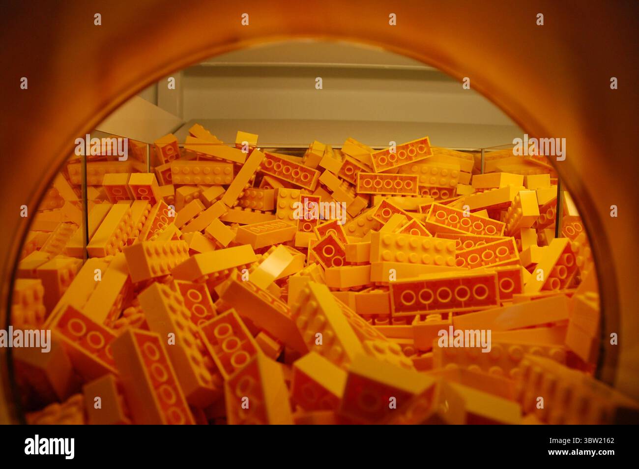 Nahaufnahme eines gelben LEGO-Backsteinbehälters an der Pick-a-Brick-Wand eines LEGO Stores mit leuchtenden Kunststoffbausteinen in einem orangefarbenen Display Stockfoto