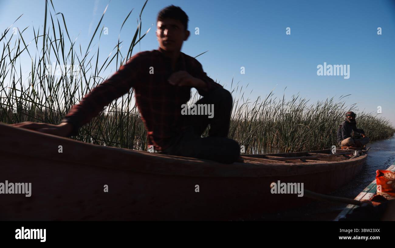 Zwei Individuen navigieren bei klarem Wetter durch die ruhigen Wasserstraßen der mesopotamischen Marschen im Irak und zeigen traditionelle Kanufahrten. Stockfoto