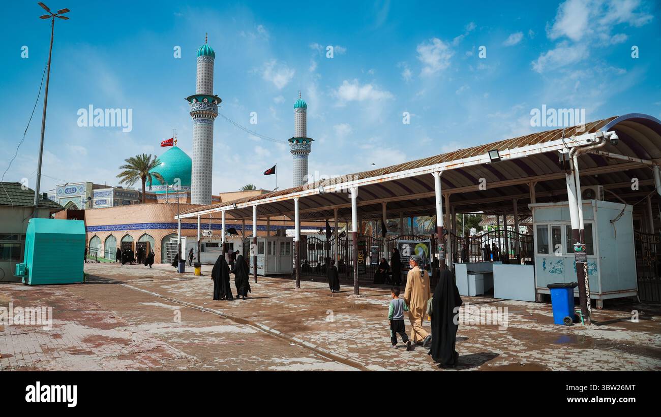 Besucher nehmen an einem bemerkenswerten Ort in Kufa, Irak, unter hellem Himmel und inmitten historischer Architektur an religiösen Aktivitäten Teil. Stockfoto