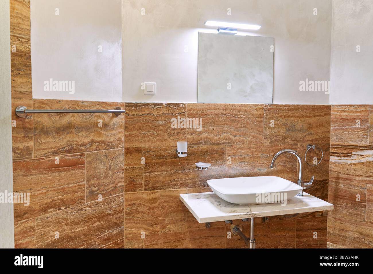 Ein modernes Badezimmer mit wunderschönen Marmorwänden und einem eleganten Waschbecken, das durch helle Beleuchtung hervorgehoben wird. Das elegante Design spiegelt einen minimalistischen und soph wider Stockfoto